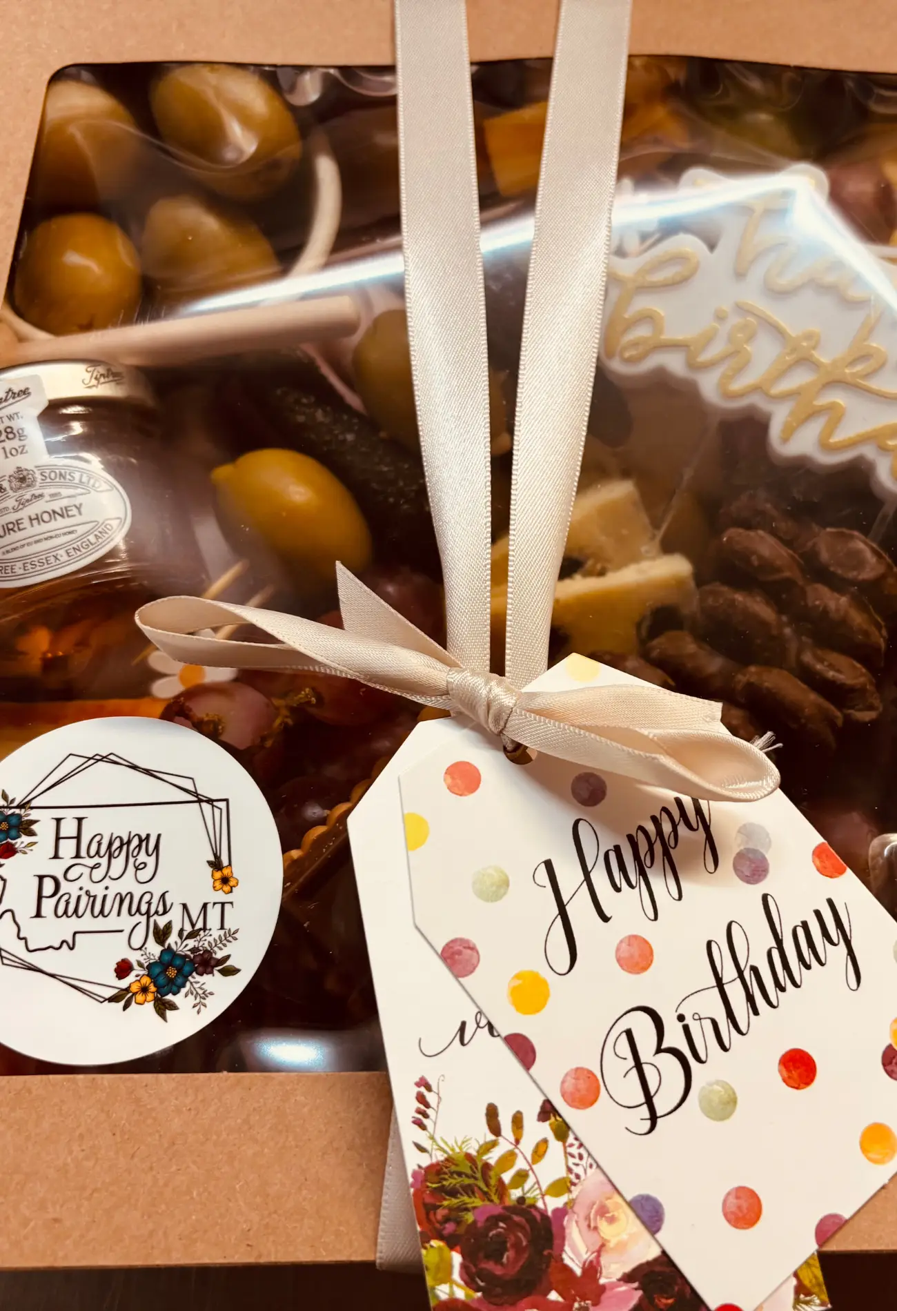 mini charcuterie box with meats, cheese, honey and chocolates wrapped up in a brown box with a bow and a Happy Pairings MT sticker